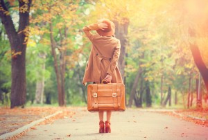 Redhead girl with suitcase in the autumn park.