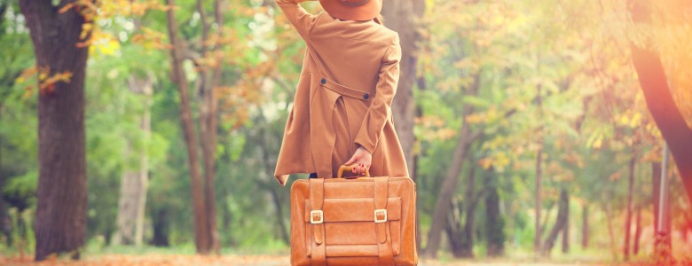 Redhead girl with suitcase in the autumn park.